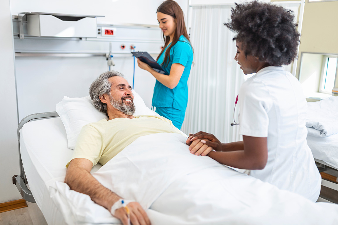 Clinical trial room with patient in bed while doctor speaks with him and nurse makes notes.