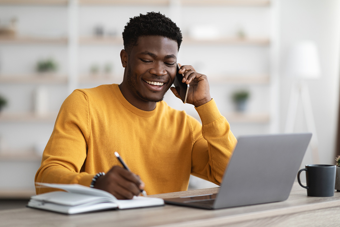 Young male talking on a mobile phone while writing notes.