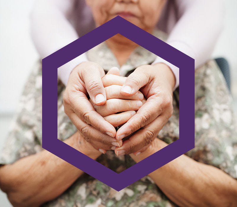 Younger female holding hands of an elderly female. The hands are enclosed in a PPD purple hexagon.