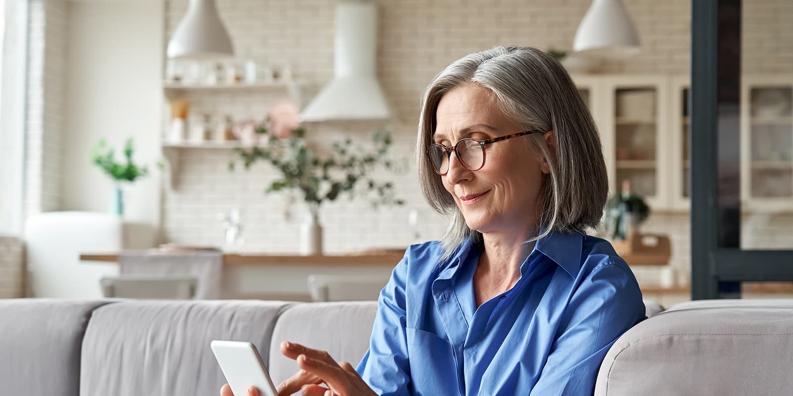 Mature woman with glasses interacting with smartphone while sitting on couch